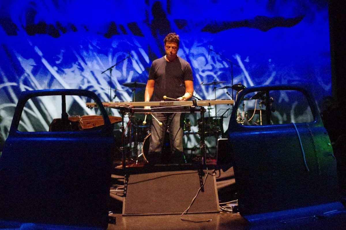 Steve Joslin playing drums with a red-lit backdrop